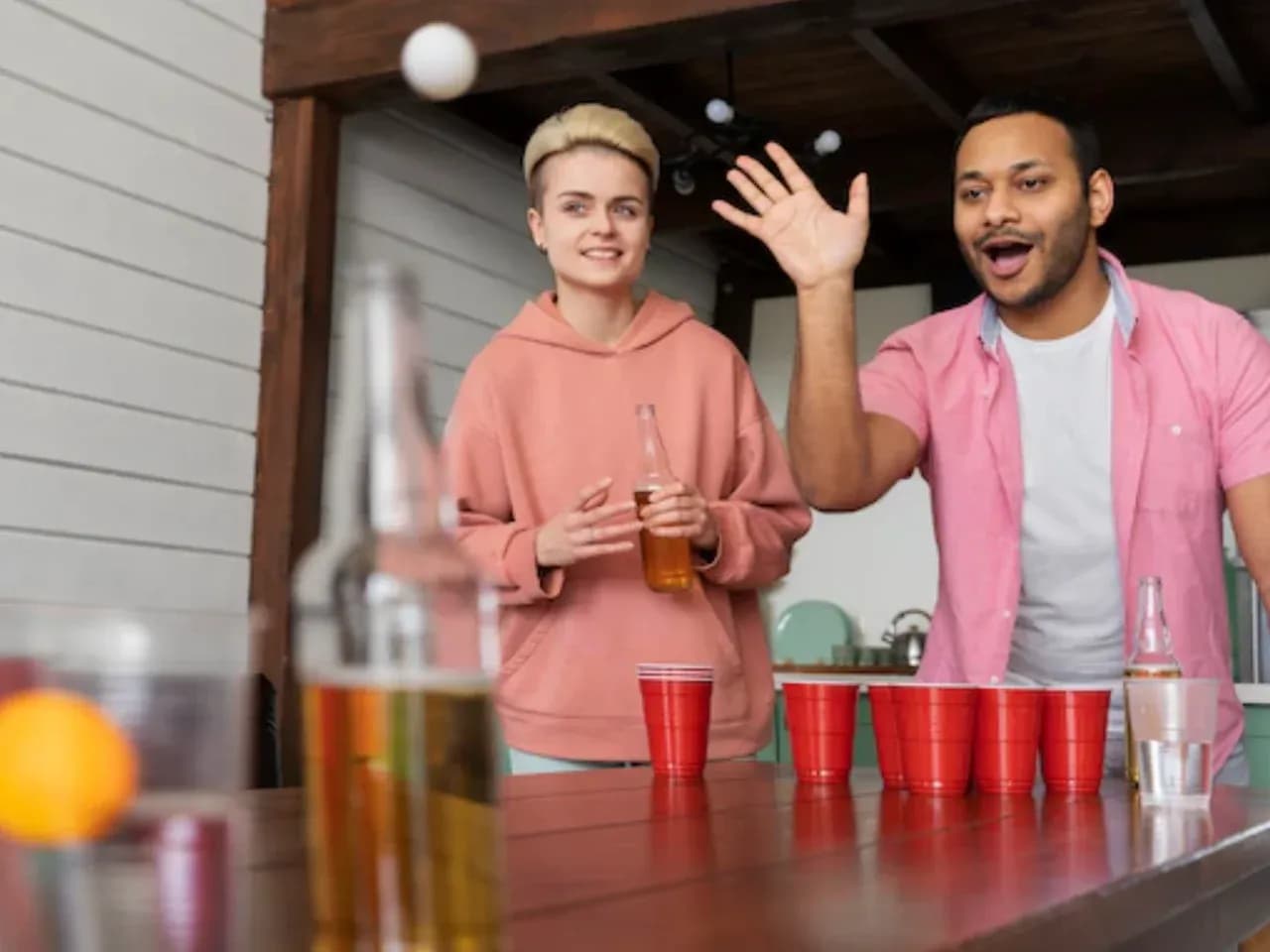 Друзья играют в Beer Pong: бросок мяча в стаканы на столе
